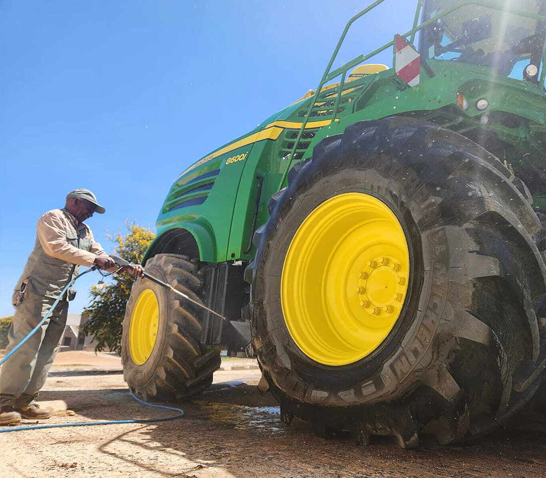 Operator washing a John Deere forage harvester with a Kränzle high pressure cleaner